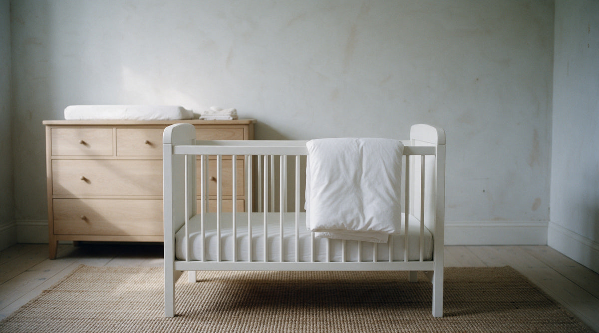 White wooden cot bed in a calm, empty nursery with a small white duvet folded over the end rail