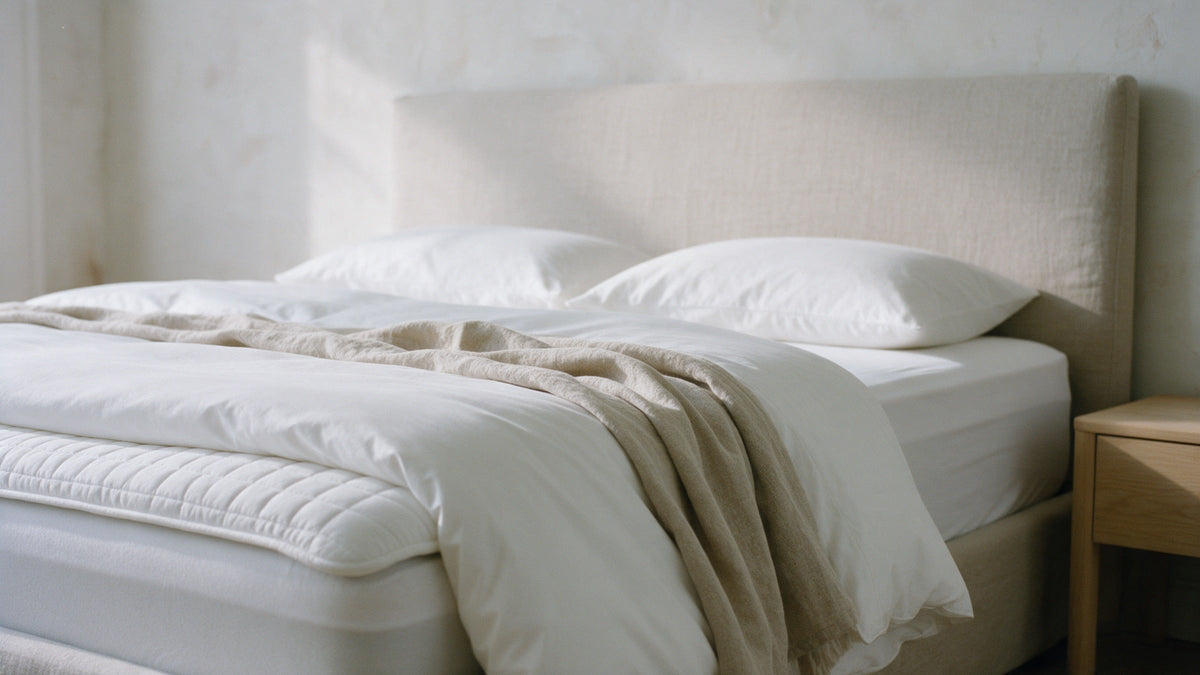 Neatly made bed seen from the foot, showing the topper, fitted sheet, turned-down duvet and pillows