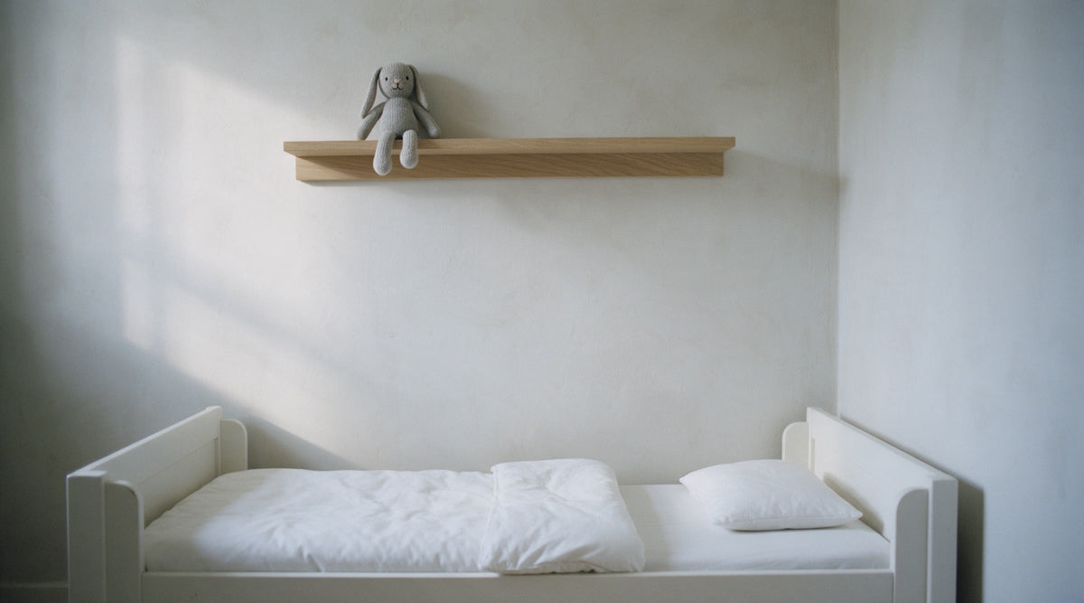 Low white toddler bed with a small white duvet folded back in a calm, empty child's bedroom