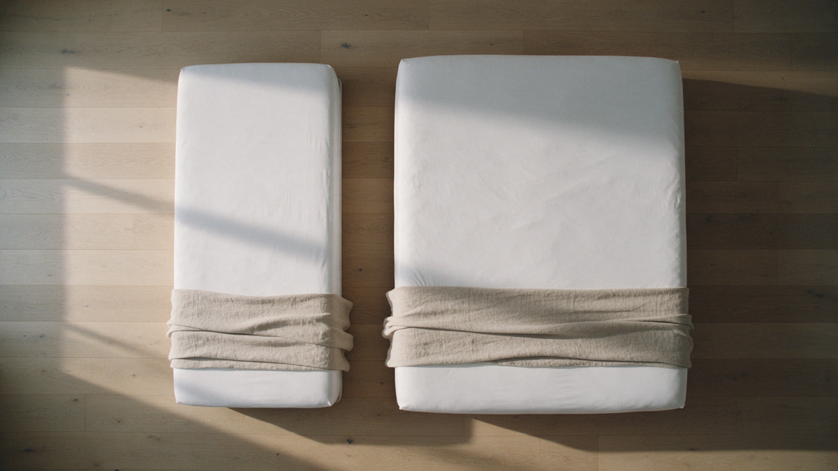 Overhead view of a single bed and a king size bed side by side with white fitted sheets on oak floorboards